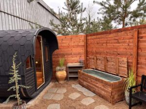 Oversigtsbillede af et udendørs spaområde med en sort tøndesauna, et udendørs spabad/jacuzzi og et koldvandsbad.