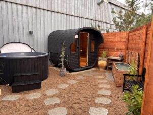 Oversigtsbillede af et udendørs spaområde med en sort tøndesauna, et udendørs spabad/jacuzzi og et koldvandsbad.